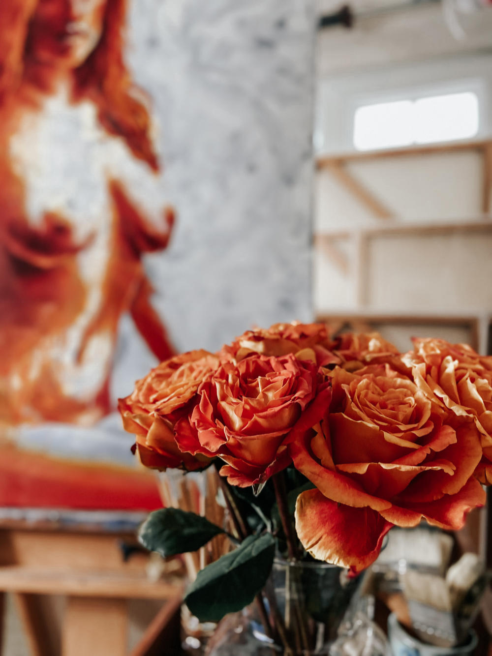 In studio photo of orange roses with painting title "I am ascendant" in background